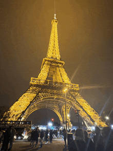 the eiffel tower is lit up at night and people are gathered around it