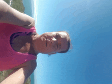 a woman in a pink tank top is taking a selfie with the ocean in the background