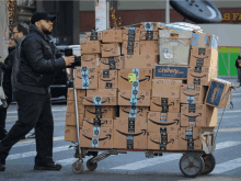 a man pushes a cart full of amazon boxes on the street