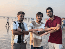 three young men standing on a beach with their arms crossed and one wearing a red shirt with the letter g on it