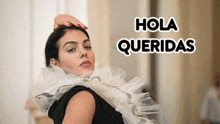 a woman wearing a black dress and a white ruffled collar with the words hola queridas written above her .