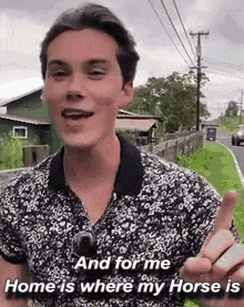 a young man in a floral shirt is standing on the side of a road and giving the middle finger .