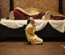 a man is kneeling in front of a bed with a person laying on it