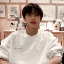 a young man wearing a white t-shirt is sitting in front of a shelf with a vase on it .