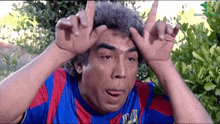 a man in a blue and red shirt is making a funny face while holding his hands to his head .