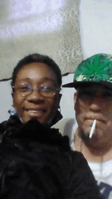 a man is smoking a cigarette next to a woman wearing glasses and a green hat .