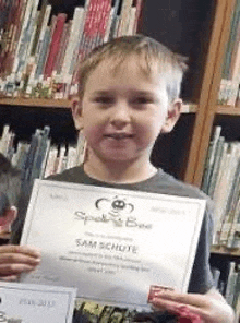 a young boy is holding a certificate in front of a book shelf .