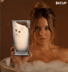 a woman in a bathtub holds a glass with a cat inside of it