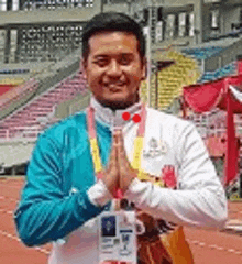 a man in a blue jacket and white shirt is standing on a track with his hands folded in prayer .