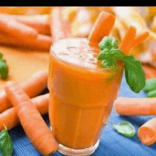 a glass of carrot juice is surrounded by carrots and basil leaves .