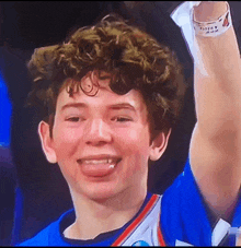 a young man with curly hair is smiling and holding his hand up