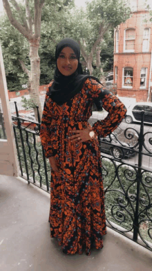 a woman wearing a hijab and a long dress stands in front of a wrought iron railing