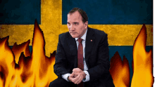 a man in a suit and tie sits in front of a swedish flag with flames behind him