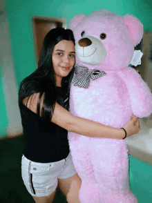 a woman holds a large pink teddy bear with a bow on it