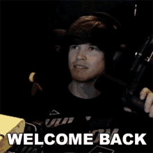 a man is holding a gun in front of a microphone and the words welcome back are on the screen .