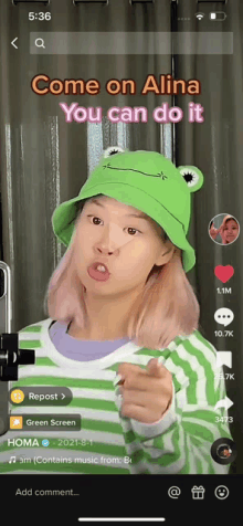 a girl wearing a frog hat is pointing at the camera