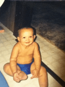 a baby wearing blue swim trunks is sitting on the floor