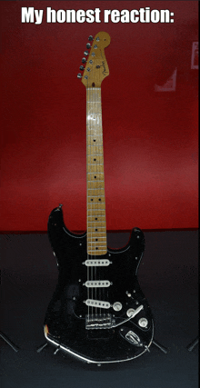 a black fender electric guitar is displayed in front of a red wall