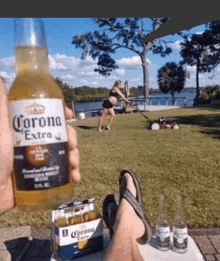 a person is holding a bottle of corona extra in front of a pregnant woman mowing the grass