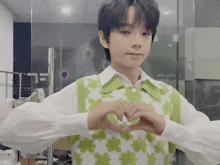 a boy in a green and white vest makes a heart shape with his hands