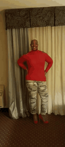 a woman in a red sweater and camo pants is standing in front of a window