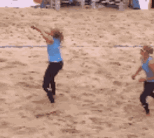 two women walking on a sandy beach with one wearing a blue tank top that says ' volleyball ' on it