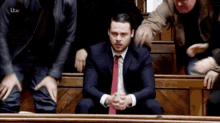 a man in a suit and tie is sitting in a courtroom surrounded by other men with itv written on their shirts