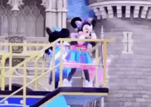 mickey mouse and minnie mouse are standing on a balcony in front of a castle .