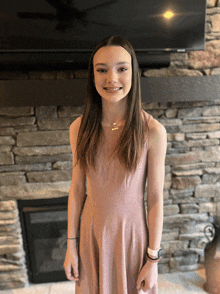 a girl in a pink dress is standing in front of a fireplace