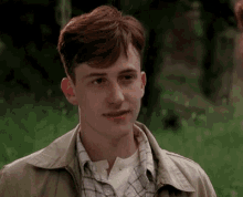 a young man with red hair is wearing a plaid shirt and tan jacket