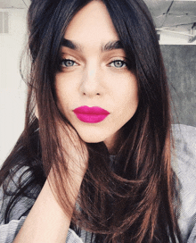 a woman with long dark hair and bright pink lipstick looks at the camera