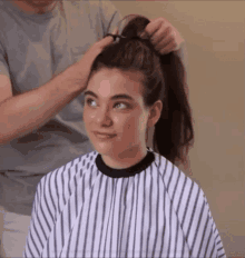 a woman wearing a striped cape is getting her hair done by a man