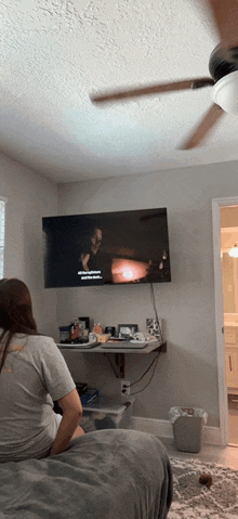 a woman is sitting on a bed watching a tv show