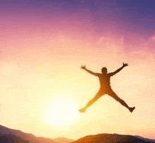 a man is jumping in the air with his arms outstretched at sunset .