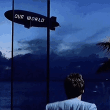 a man stands in front of a zeppelin that says our world