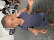 a little boy in a blue shirt is standing on a gray carpet