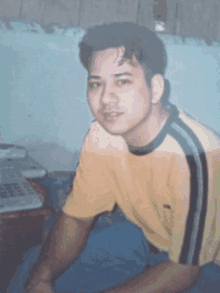 a young man in a yellow shirt sits in front of a keyboard