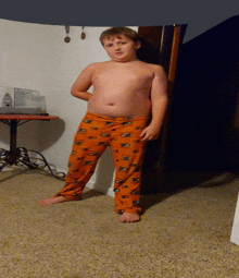 a boy without a shirt is standing in a room wearing orange pajama pants