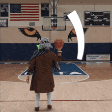 an older woman is holding a basketball on a basketball court with a central academy asics sign in the background