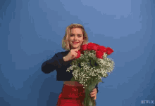 a woman is holding a bouquet of red roses and baby 's breath in front of a blue wall that says netflix