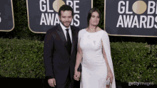 a man in a suit and tie stands next to a woman in a white dress on a red carpet