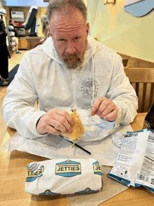 a man sitting at a table eating a sandwich from jetties