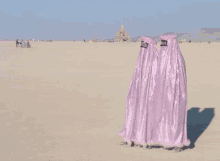 three people are standing in the middle of a desert wearing pink dresses .