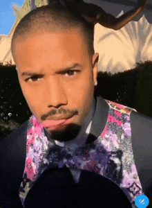 a man wearing a floral vest and bow tie is making a face