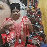 a woman is sitting at a table with a christmas tree in the background holding a bag of coca cola .