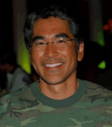 a man wearing glasses and a camouflage shirt is smiling for the camera