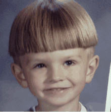 a young boy with a very short hairstyle smiles for the camera