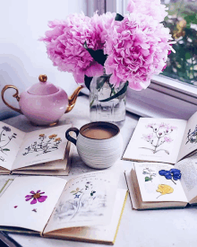 a cup of coffee sits on a table next to a vase of pink flowers and botanical books