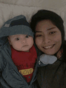 a woman is holding a baby who is wearing a red shirt that says love