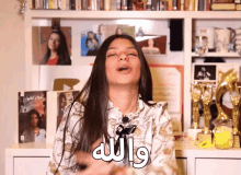 a woman stands in front of a shelf full of books and awards with arabic writing on the front of her shirt